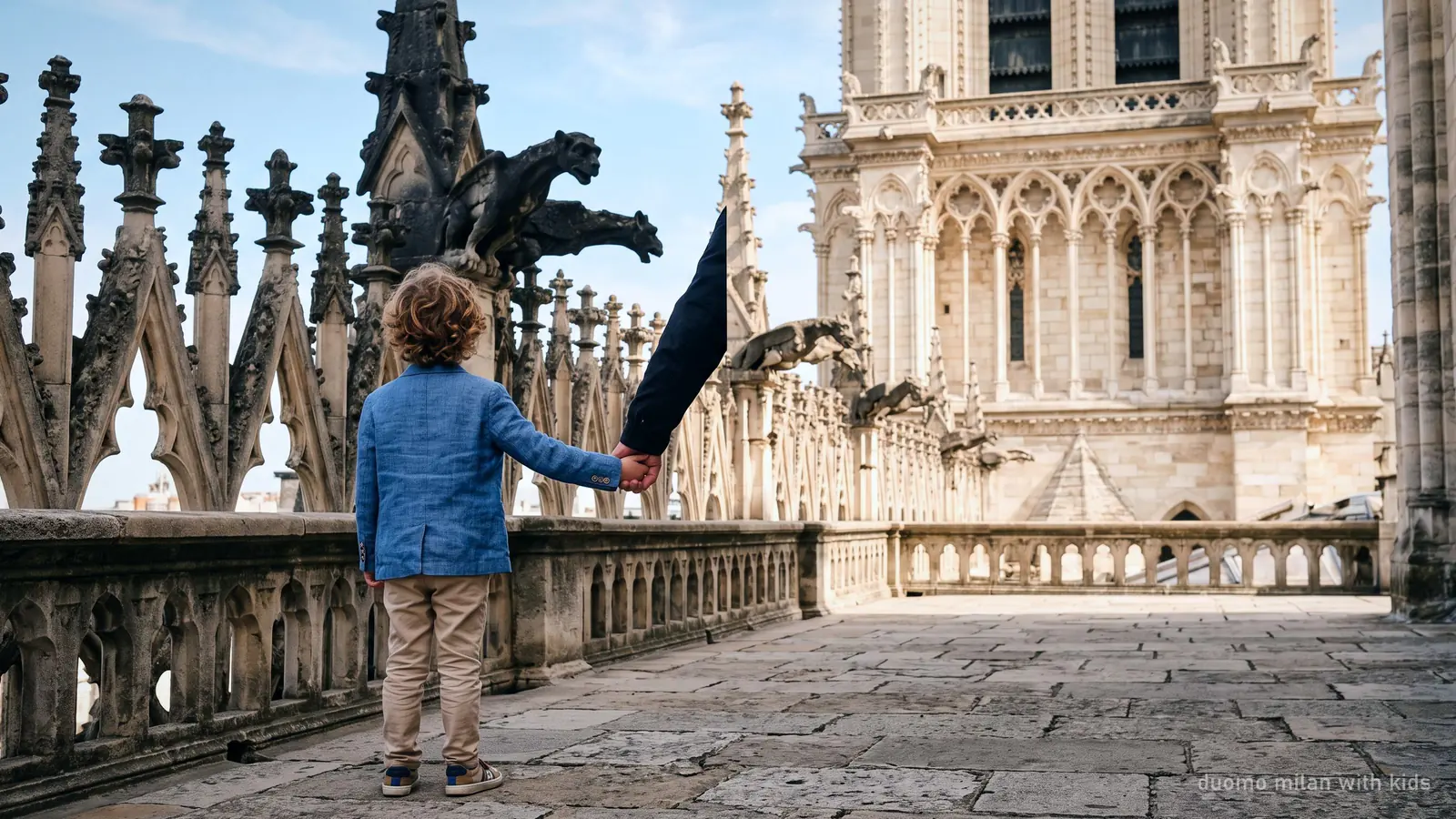A child on the Duomo Milan roof terrace looking up at the carved stone gargoyles, holding an adult's hand