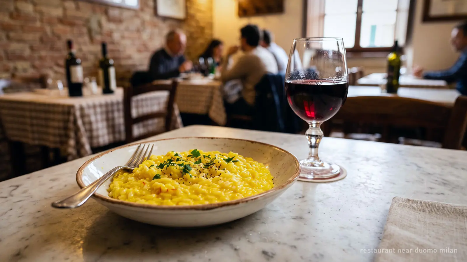 A plate of risotto alla milanese and a glass of red wine on a marble table in a Milanese trattoria